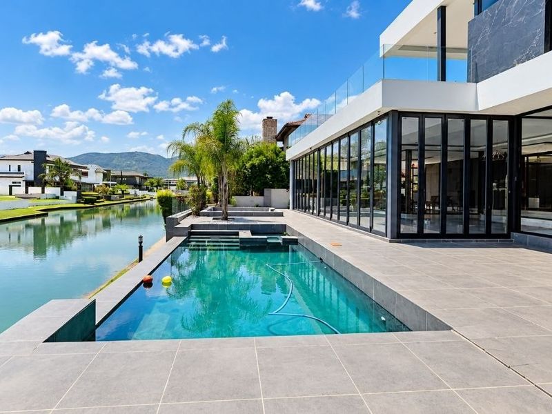 Modern waterfront property featuring a sleek swimming pool, expansive tiled patio, and large glass bi-fold doors overlooking the canal.