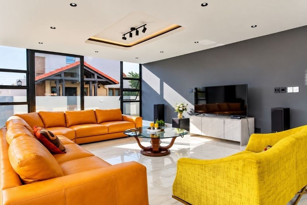 A modern, well-lit living room featuring large format floor tiles, a coffered ceiling with recessed lighting, and expansive aluminium-framed glass doors.