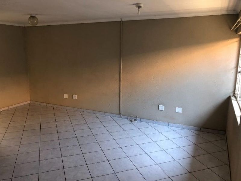 An empty living area featuring tiled flooring and exposed electrical conduit, offering a blank canvas for renovation and interior design updates.