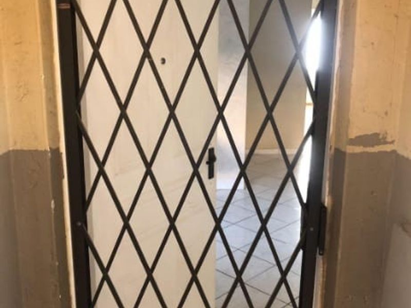 An entry area featuring a security gate and tiled flooring, showing signs of wear on the surrounding wall surfaces.