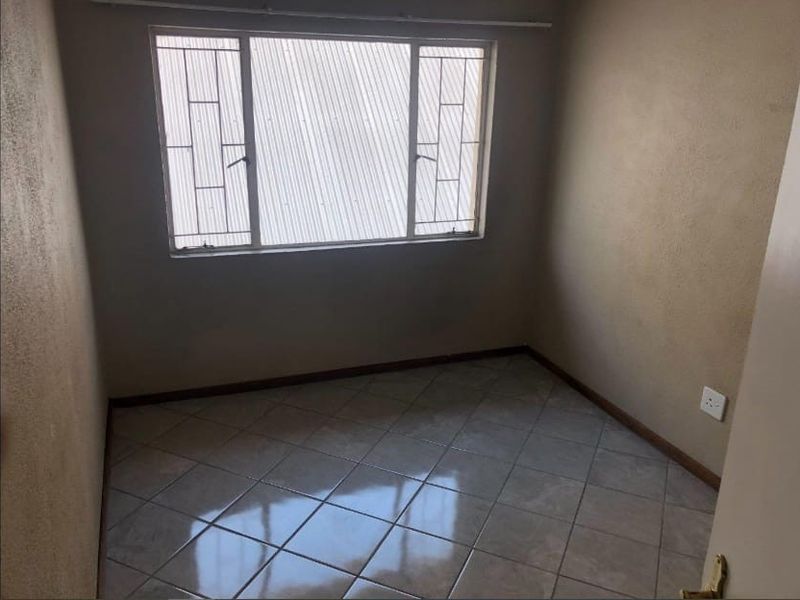 An empty bedroom featuring tiled flooring, neutral wall finishes, and a window fitted with security bars.