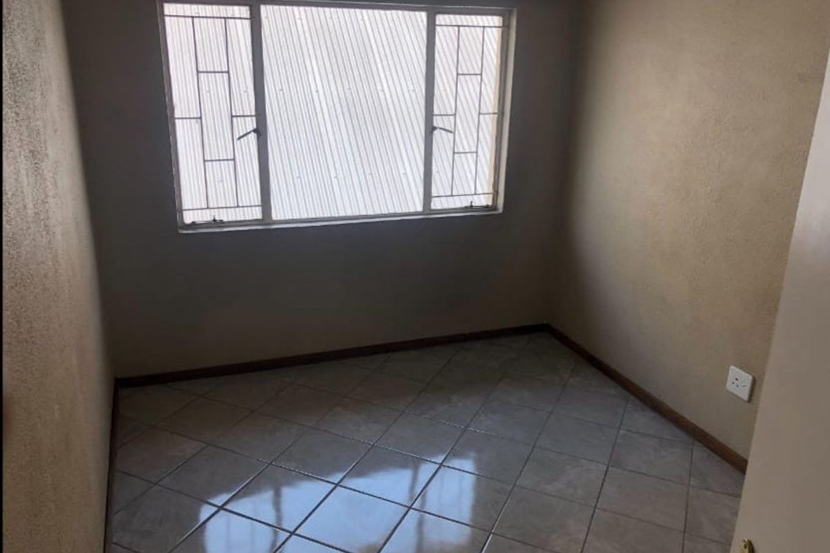 An empty bedroom featuring tiled flooring, neutral wall finishes, and a window fitted with security bars.