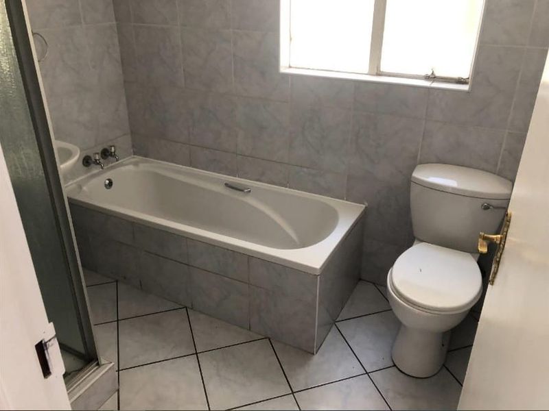 A functional bathroom featuring a bathtub, shower enclosure, and toilet with tiled finishes throughout.