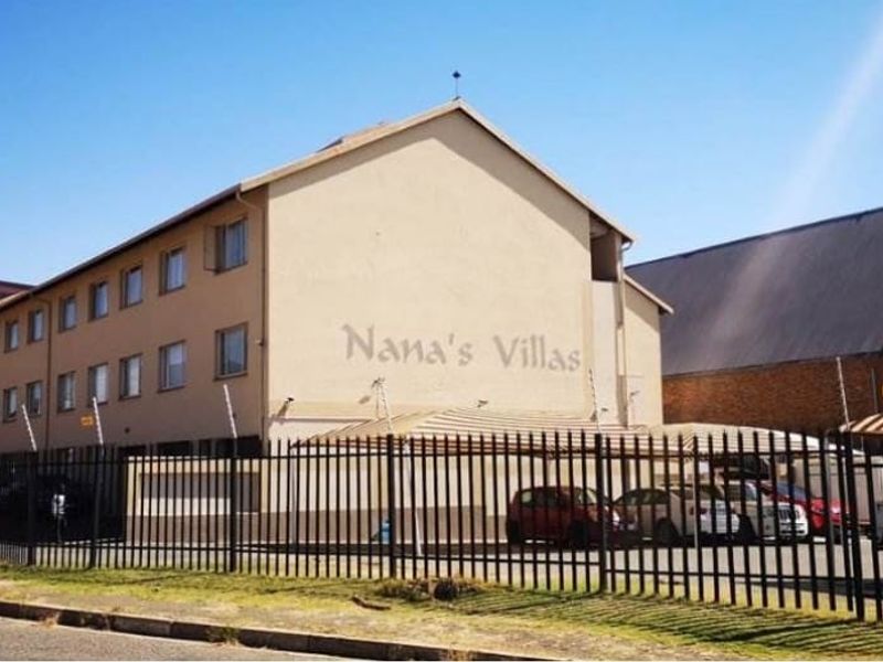 Exterior view of Nana's Villas apartment complex featuring a secure gated entrance, perimeter fencing, and covered parking facilities.