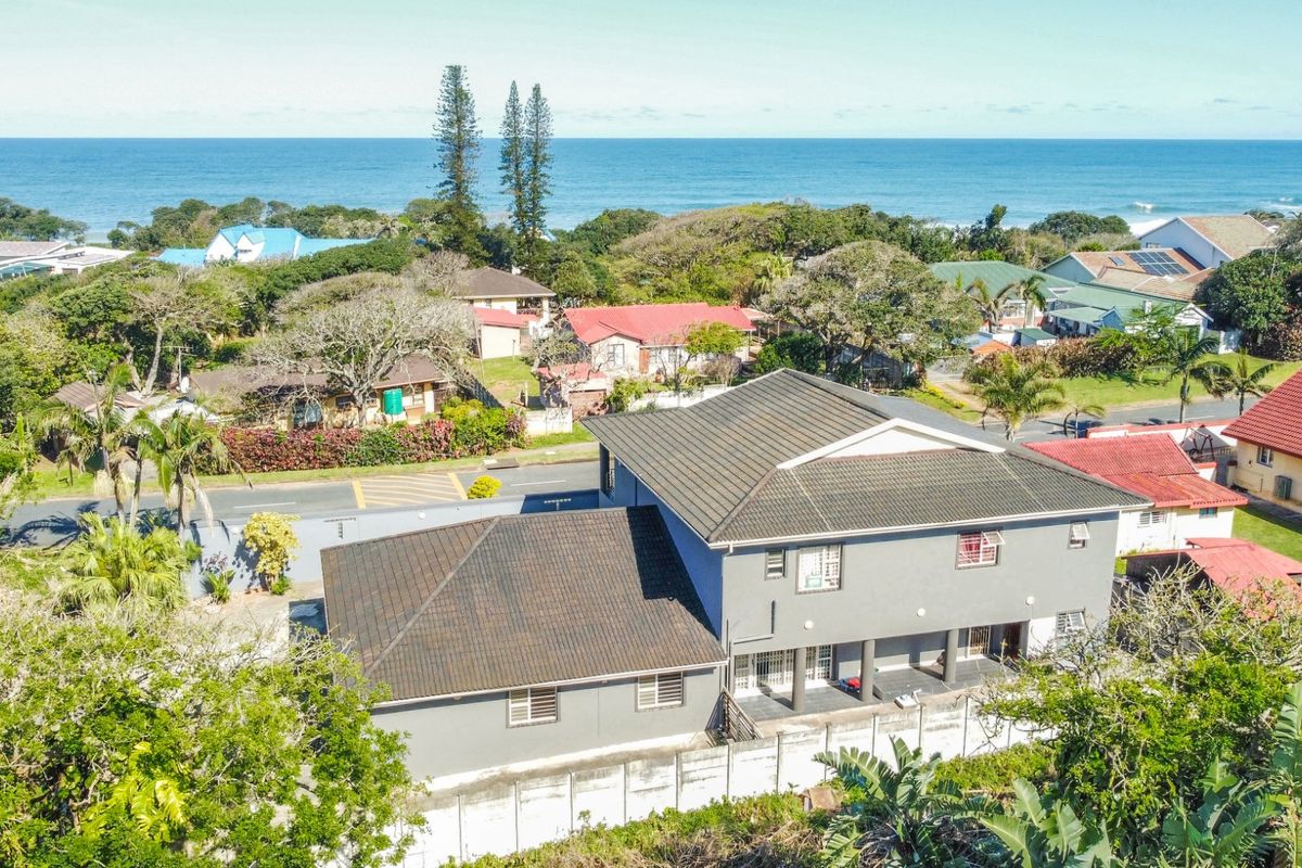 Aerial view of the property showcasing the building structure, tiled roof, surrounding garden, and coastal neighborhood setting.