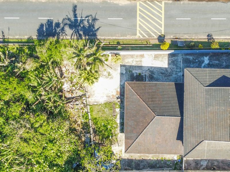 Aerial view of the property showing the roof structure, concrete driveway, and surrounding garden area with mature trees and boundary wall.