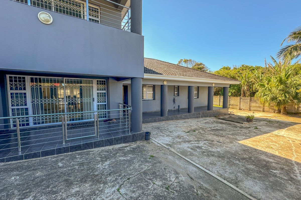 Rear exterior view of the house featuring a tiled patio with stainless steel balustrades, concrete driveway, and established garden surroundings.