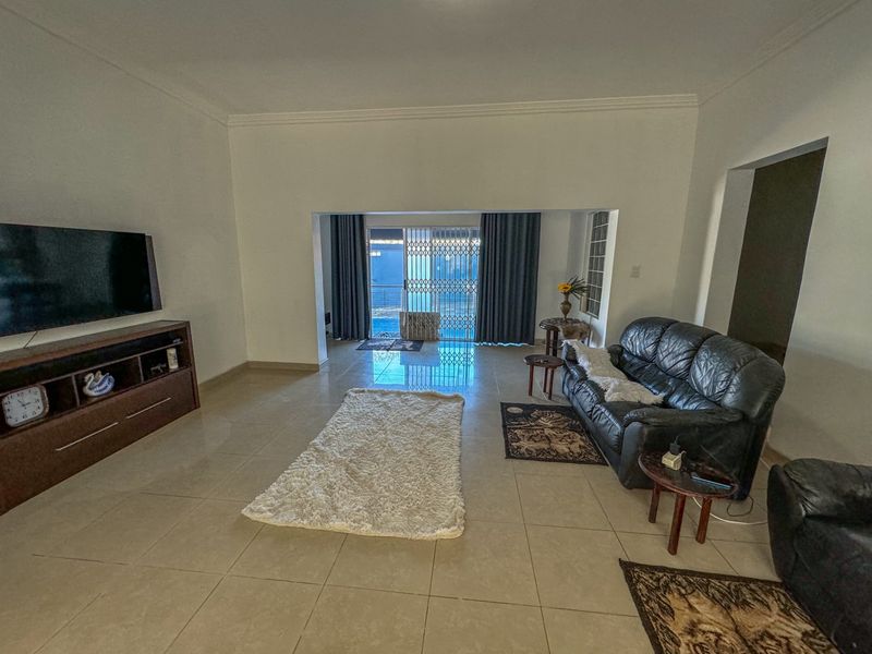 Spacious living area featuring neutral tiled flooring, coved ceilings, and a large sliding glass door providing access to the outdoor area.
