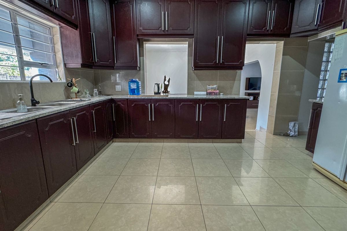 A functional kitchen featuring dark wood cabinetry, granite countertops, a double basin sink, and neutral tiled flooring with a clean, well-maintained finish.