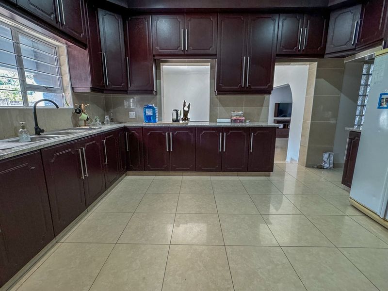 A functional kitchen featuring dark wood cabinetry, granite countertops, a double basin sink, and neutral tiled flooring with a clean, well-maintained finish.