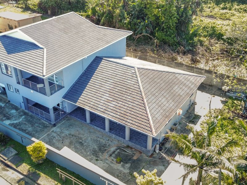 Aerial view of a two-story residential property featuring a tiled roof, covered patio area, balcony, and concrete driveway within a fenced perimeter.
