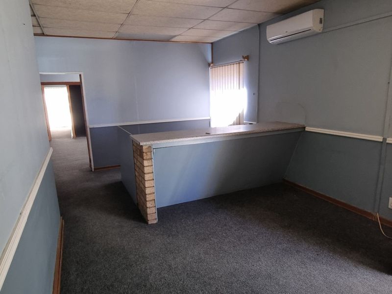 Empty office space featuring a built-in reception counter, split-system air conditioning, carpeted flooring, and a suspended ceiling, suitable for a professional workspace.