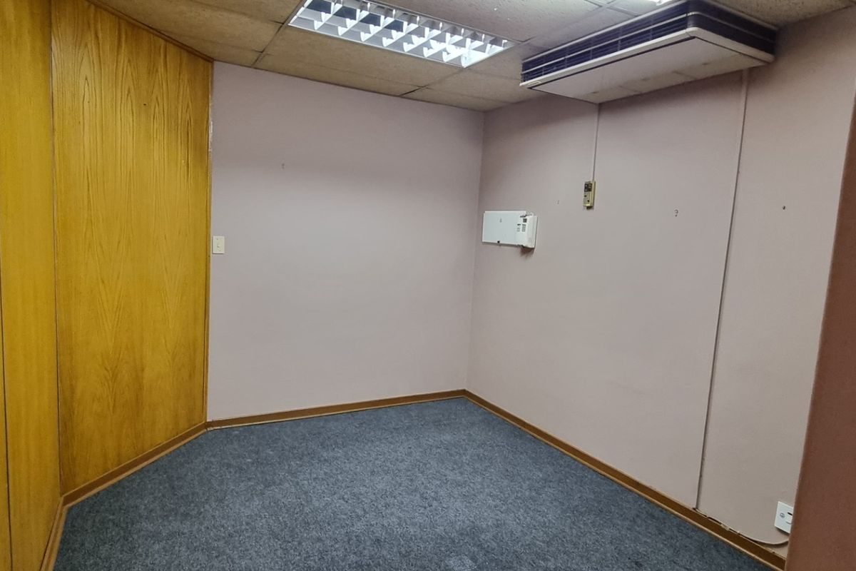 An empty office space featuring wood paneling, carpet flooring, a suspended ceiling with integrated lighting, and a wall-mounted air conditioning unit.