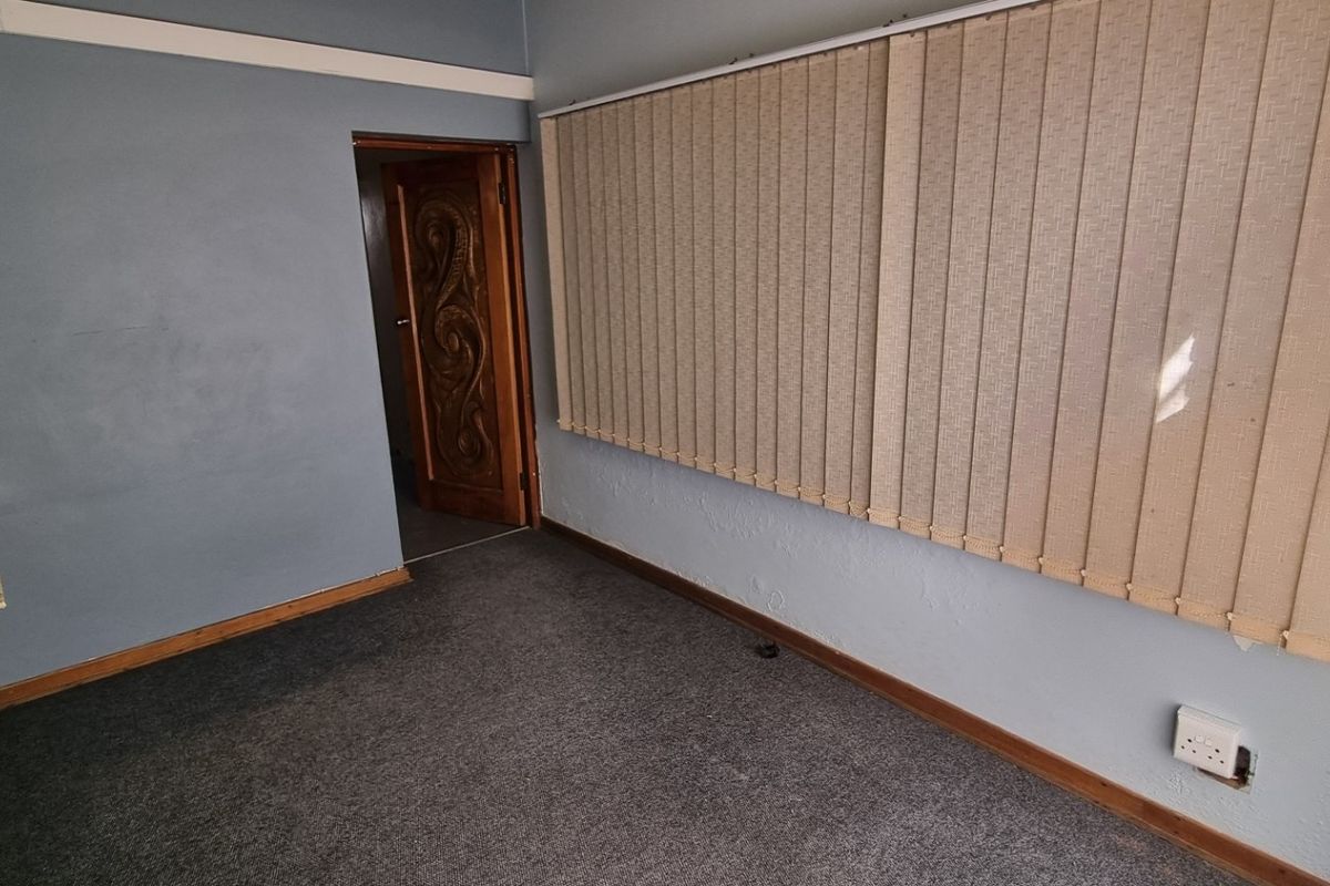 A vacant office space featuring grey carpet flooring, vertical window blinds, and a decorative timber door, requiring minor cosmetic updates.