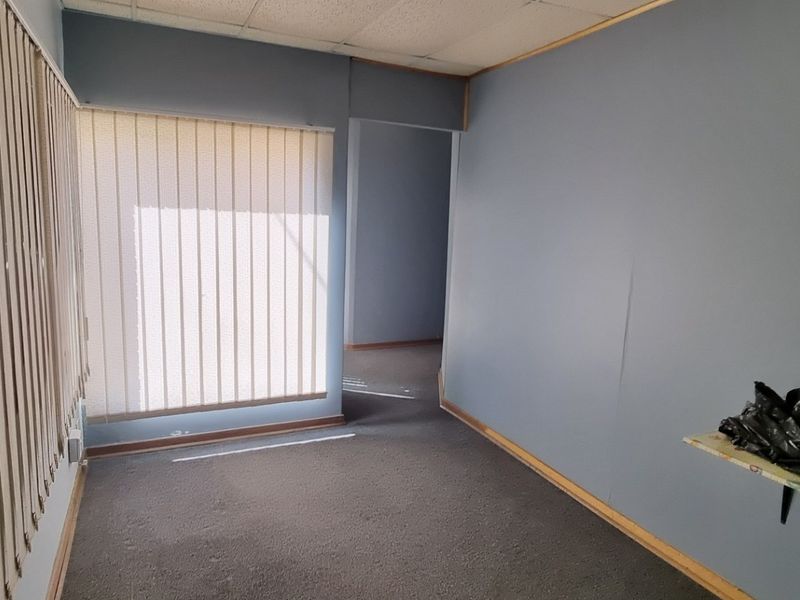 An empty office space featuring carpeted flooring, vertical blinds, and a suspended ceiling, offering a blank canvas for professional workspace customization.
