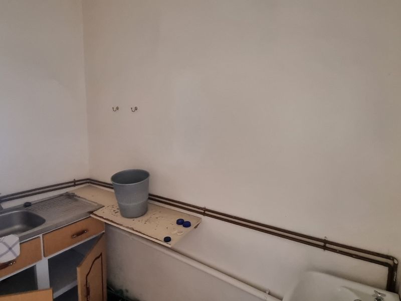 A basic utility space featuring a stainless steel sink, exposed plumbing, and built-in cabinetry, requiring cosmetic updates and maintenance.