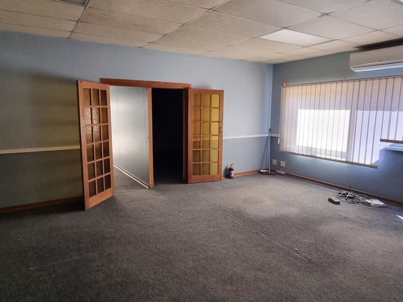 An empty office space featuring a suspended ceiling, split-system air conditioning, carpet flooring, and double french doors leading to an adjacent room.