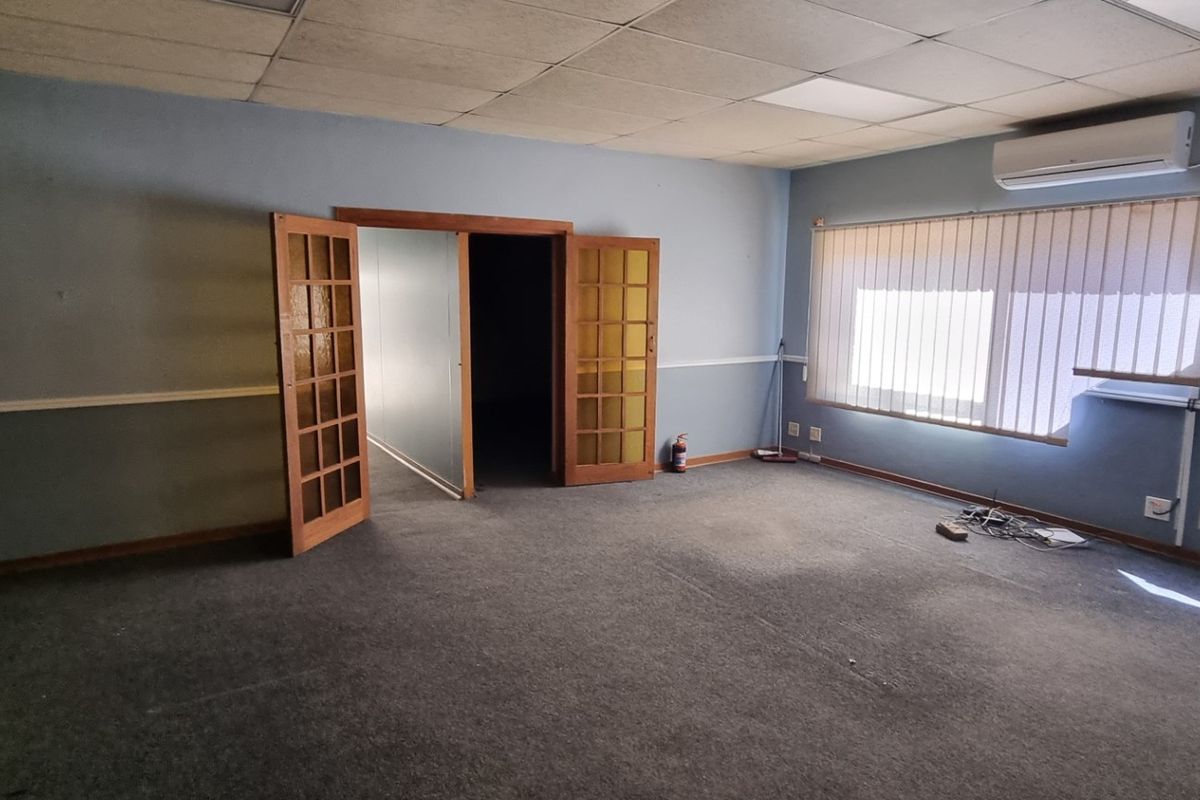 An empty office space featuring a suspended ceiling, split-system air conditioning, carpet flooring, and double french doors leading to an adjacent room.