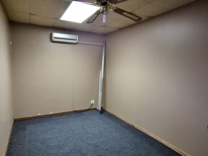 A vacant office space featuring a drop ceiling, ceiling fan, split-system air conditioning unit, and carpeted flooring.