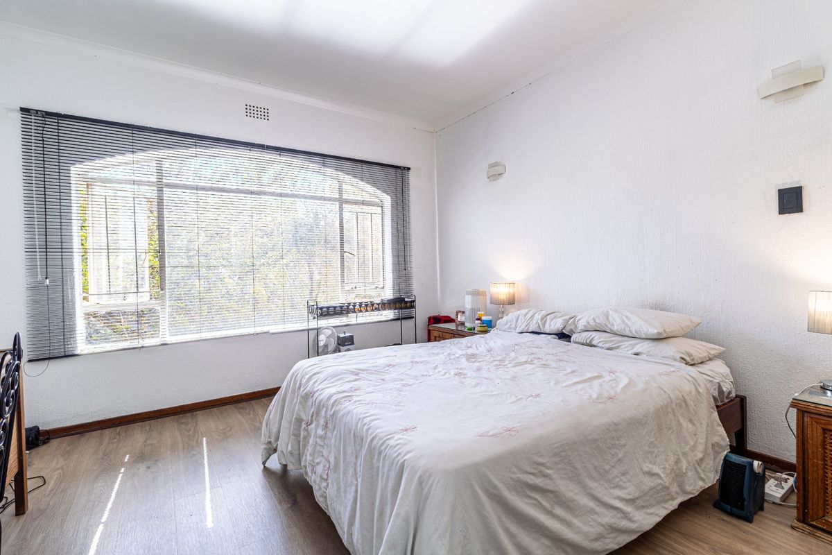 A bedroom featuring laminate flooring, an arched window with venetian blinds, and wall-mounted lighting fixtures.