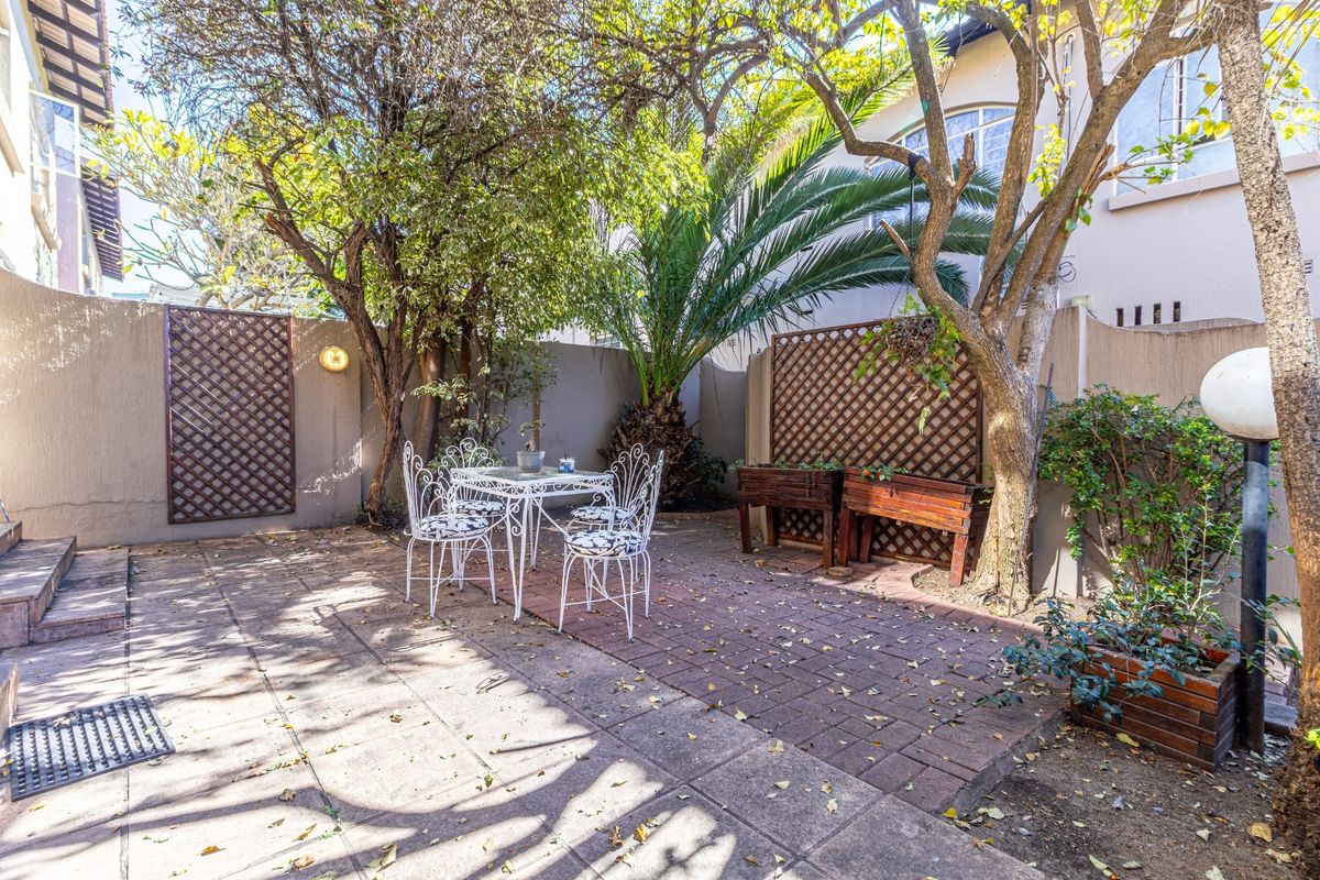 A private rear courtyard featuring paved flooring, boundary walls with decorative trellis panels, and established trees, providing a quiet outdoor entertainment space.