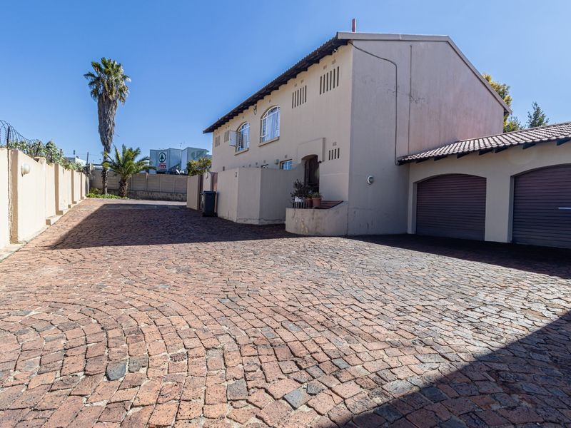 Exterior view of a townhouse featuring a large cobblestone driveway, double garage, and perimeter wall with security fencing.