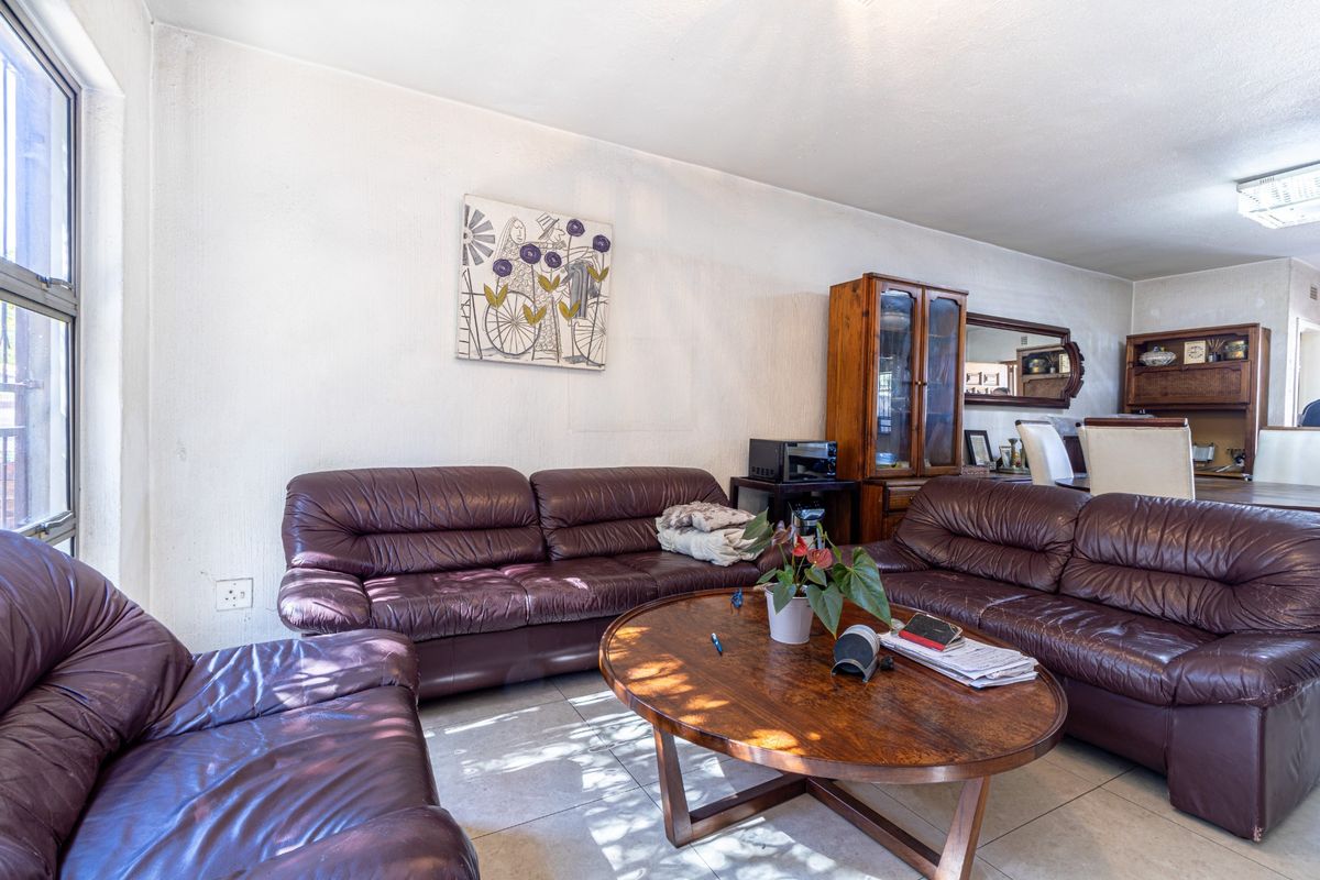 A living room area featuring tiled flooring and a large window, showing signs of wear on the wall surfaces.