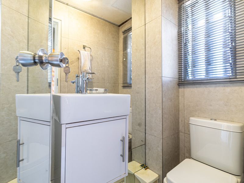A compact, modern bathroom featuring full-height wall tiling, a sleek vanity cabinet with a chrome mixer tap, and a standard toilet.