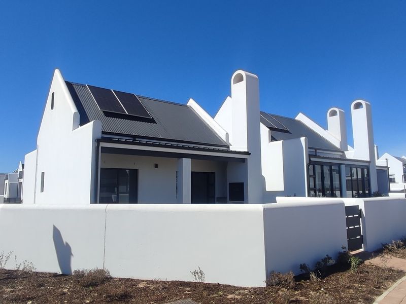 Modern white house exterior featuring a metal roof with integrated solar panels, prominent chimney stacks, and a clean perimeter wall in a residential estate.