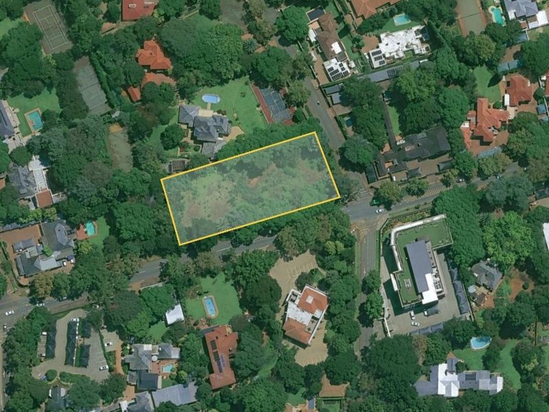 An aerial view of a vacant land plot situated within a well-established, tree-lined residential and commercial neighbourhood.