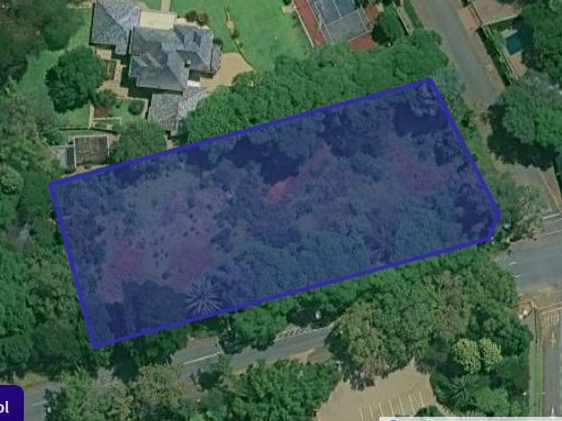 An aerial view showing a rectangular land parcel highlighted in blue, situated within a residential neighbourhood with surrounding trees and road access.