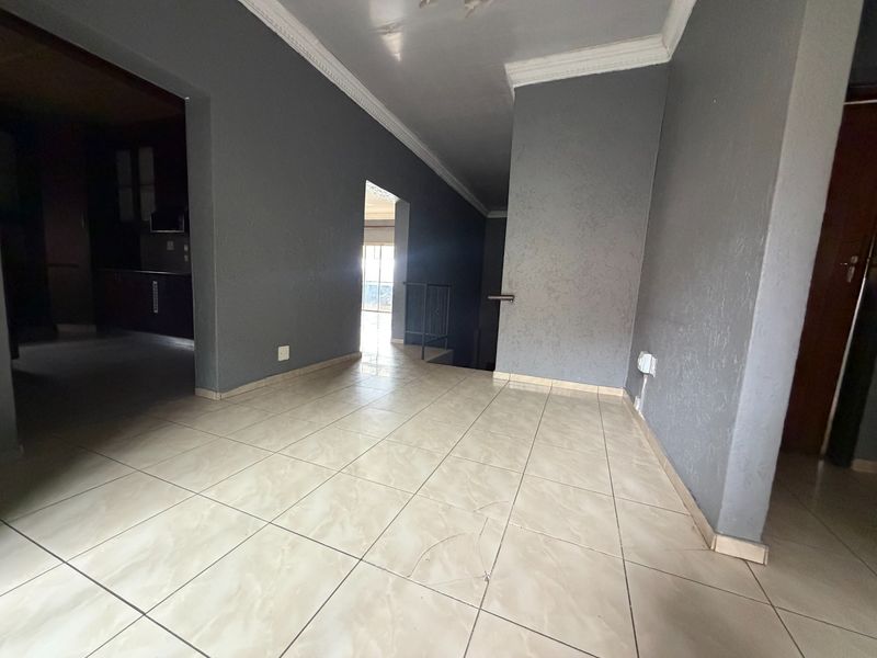 A spacious, empty hallway featuring neutral tiled flooring, grey walls with crown molding, and access to adjacent living areas and a staircase.
