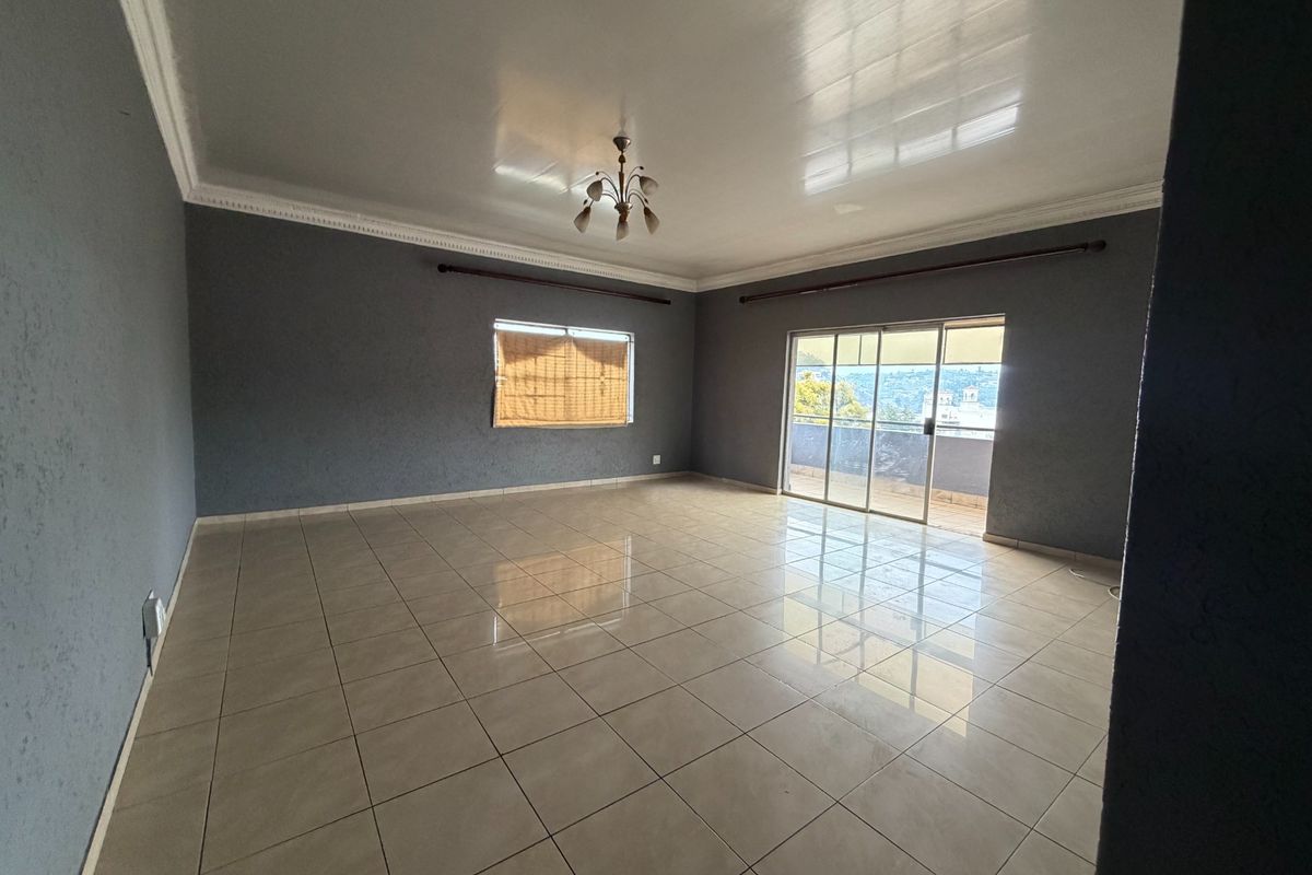 Spacious, empty living room featuring neutral tiled flooring, crown molding, and a sliding glass door leading to an outdoor area.