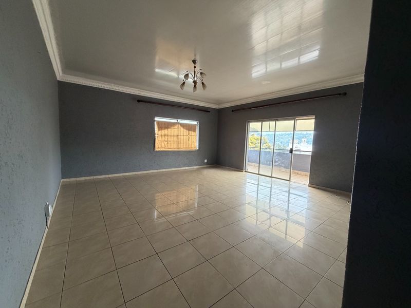 Spacious, empty living room featuring neutral tiled flooring, crown molding, and a sliding glass door leading to an outdoor area.