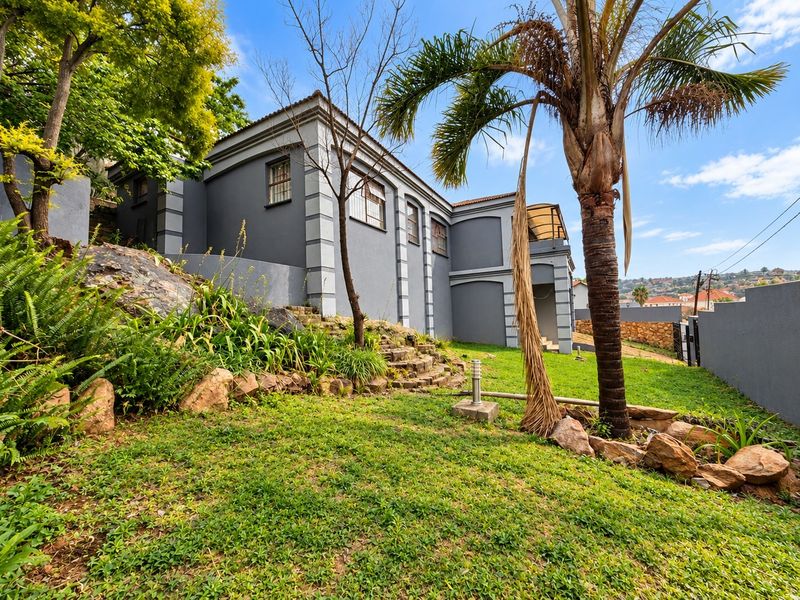 A view of the rear exterior of the house featuring a landscaped garden, stone retaining wall, and perimeter boundary wall.