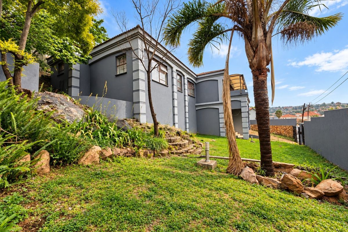 A view of the rear exterior of the house featuring a landscaped garden, stone retaining wall, and perimeter boundary wall.