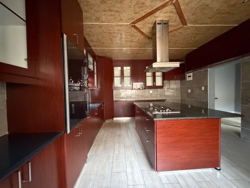 Spacious kitchen featuring dark wood cabinetry, a central island with a gas hob, granite countertops, and modern tiled flooring.