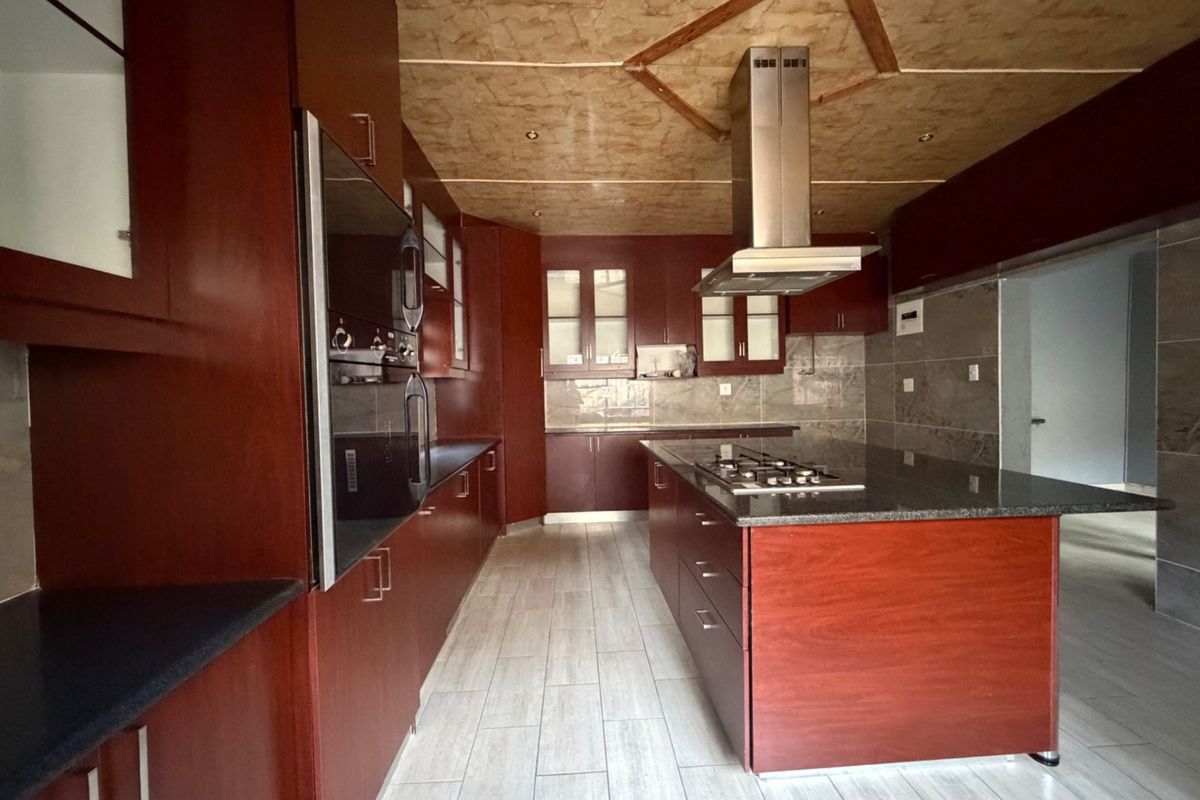 Spacious kitchen featuring dark wood cabinetry, a central island with a gas hob, granite countertops, and modern tiled flooring.