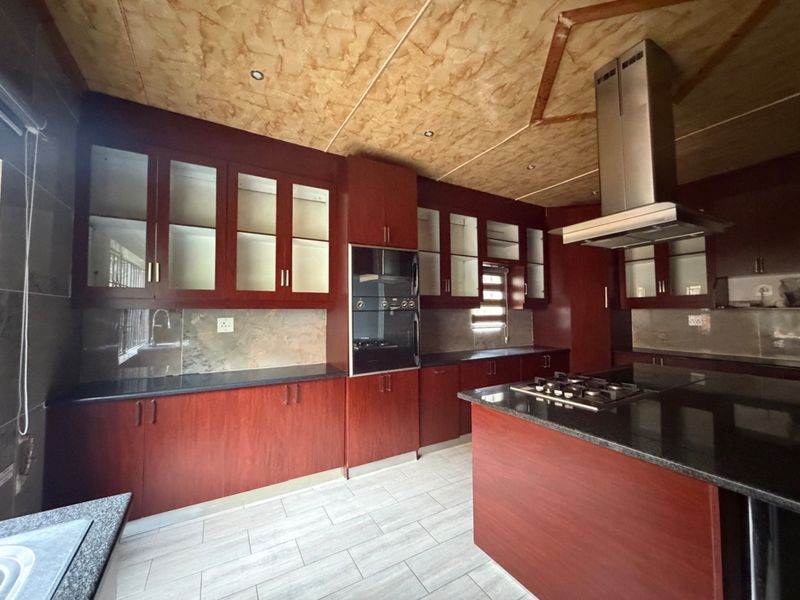 Spacious kitchen featuring dark wood cabinetry, granite countertops, built-in oven, gas hob, and extractor fan, complemented by light-toned tiled flooring.
