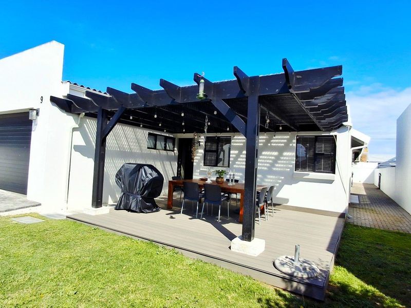 A well-maintained outdoor patio area featuring a dark timber pergola, composite decking, and direct access to the garage and main house.