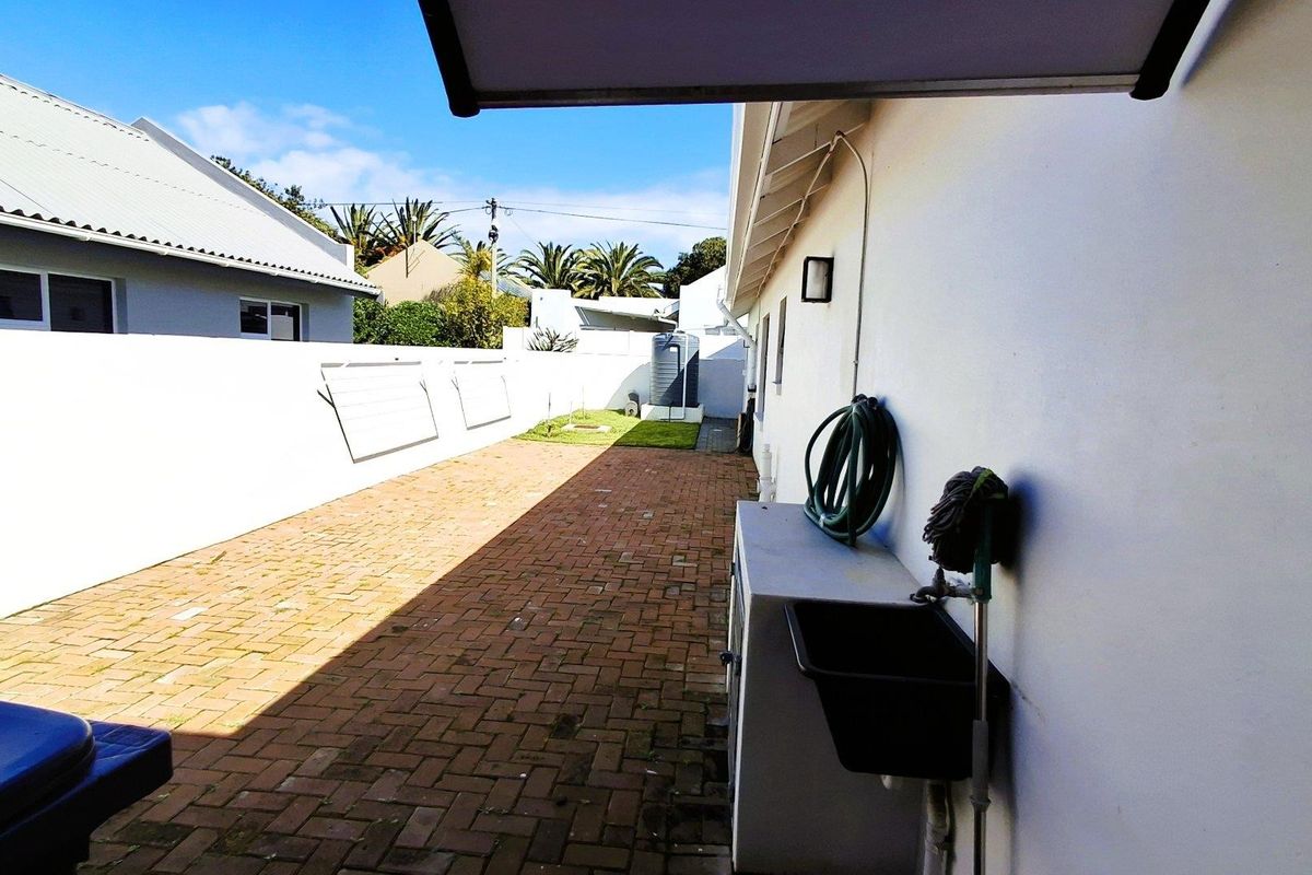 A side exterior area featuring brick paving, a boundary wall, a utility sink, and a water tank, providing functional outdoor space.