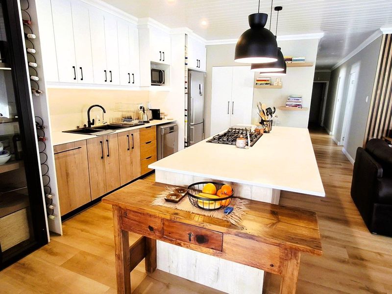 Modern open-plan kitchen featuring a large island with gas cooktop, contemporary cabinetry, and timber flooring, seamlessly flowing into the living area.