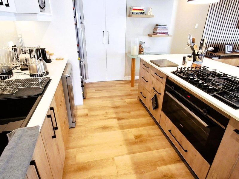 Modern kitchen featuring light wood cabinetry, stone countertops, a built-in oven with gas cooktop, and a stylish slatted wood feature wall.