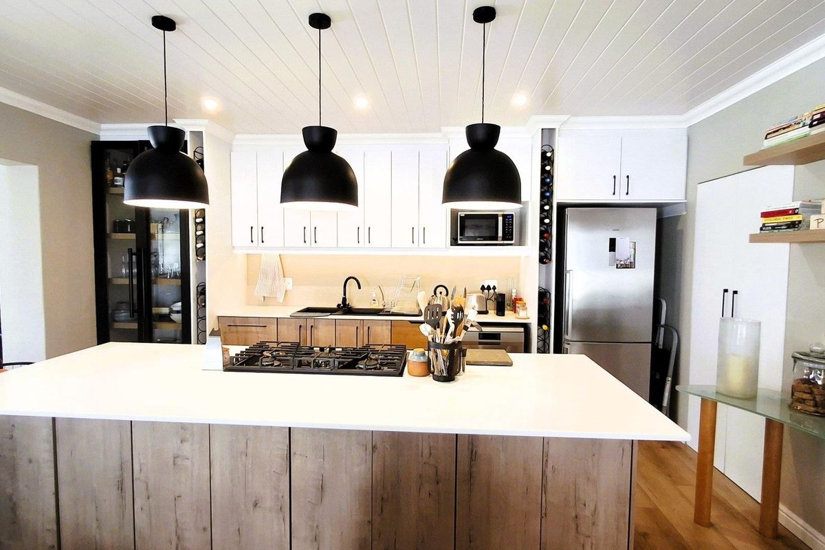 Modern kitchen featuring a large central island with gas hob, white shaker cabinetry, tongue and groove ceiling, and integrated appliances.