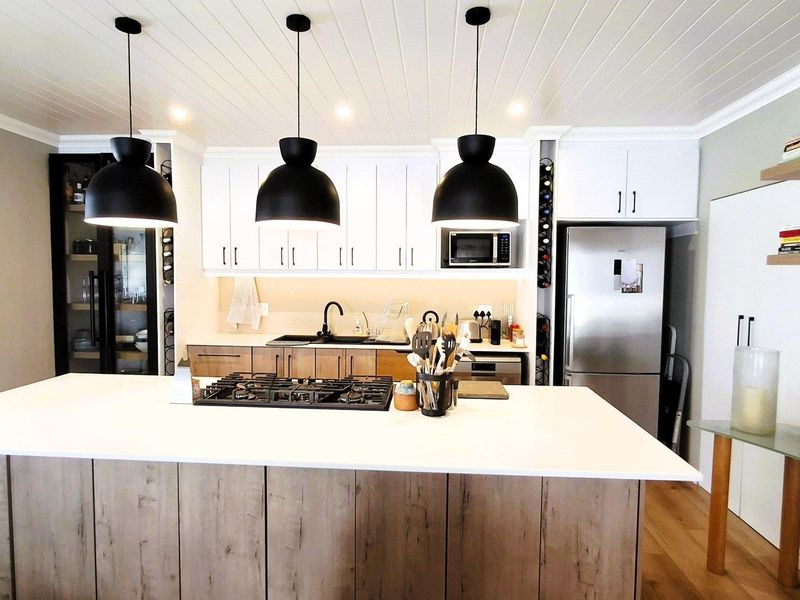 Modern kitchen featuring a large central island with gas hob, white shaker cabinetry, tongue and groove ceiling, and integrated appliances.