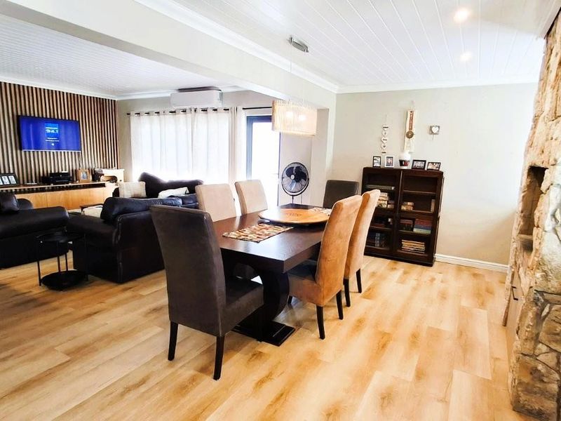 Spacious open-plan living and dining area featuring a striking stone fireplace, timber slat feature wall, and modern timber laminate flooring throughout.