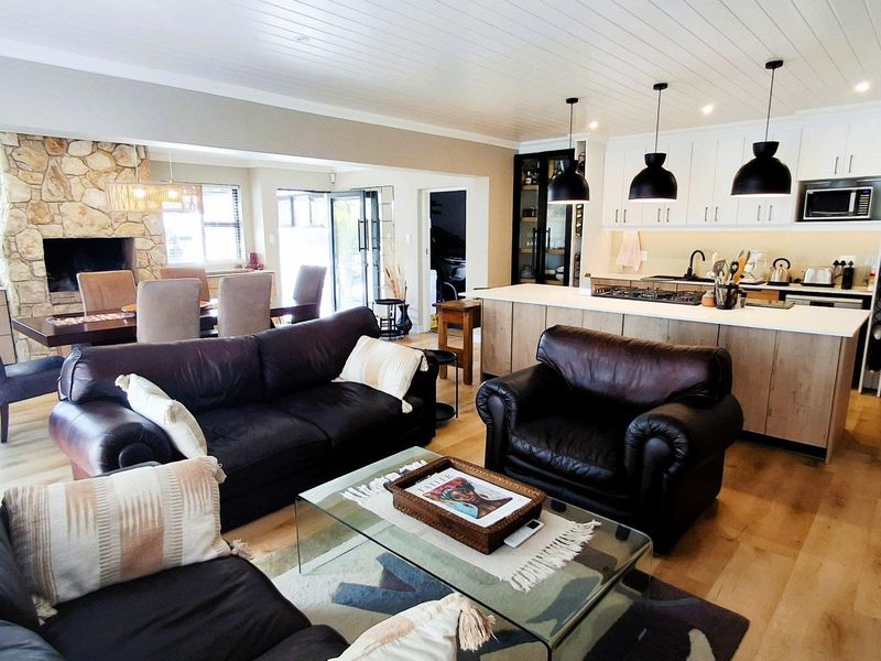 Spacious open-plan living area featuring a stone fireplace, modern kitchen with island, pendant lighting, and timber flooring throughout.