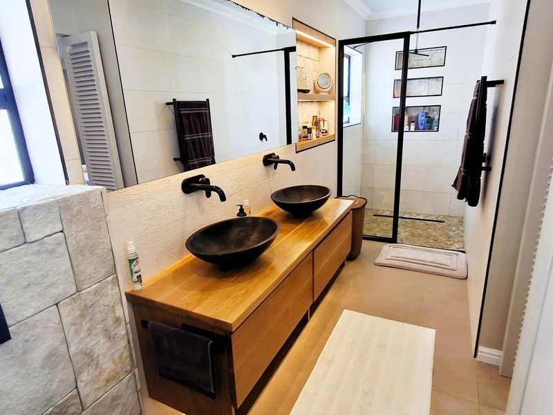 Modern bathroom featuring a double vanity with vessel sinks, wall-mounted faucets, and a spacious walk-in shower with a black frame and stone accents.
