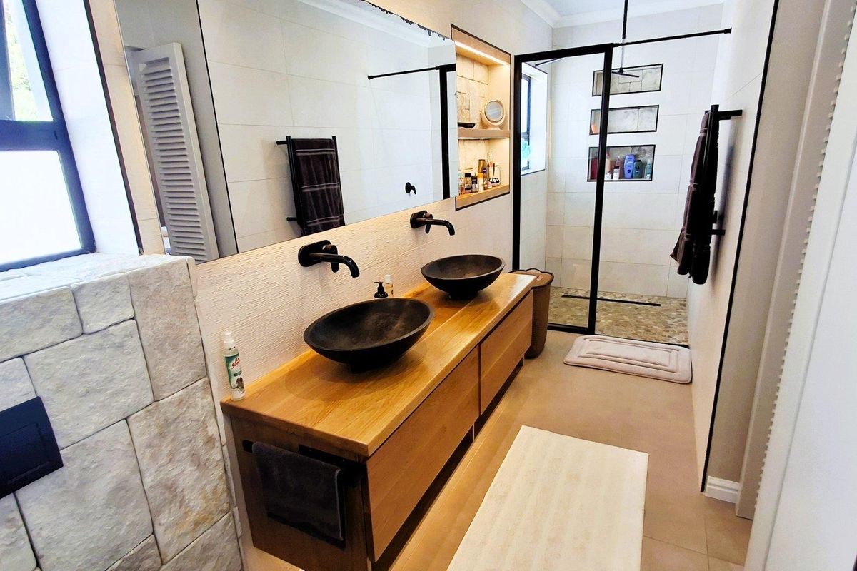 Modern bathroom featuring a double vanity with vessel sinks, wall-mounted faucets, and a spacious walk-in shower with a black frame and stone accents.