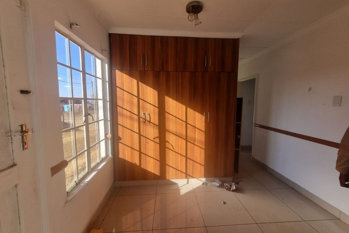 A vacant bedroom featuring built-in wooden cupboards, tiled flooring, and natural light through a window with security bars.